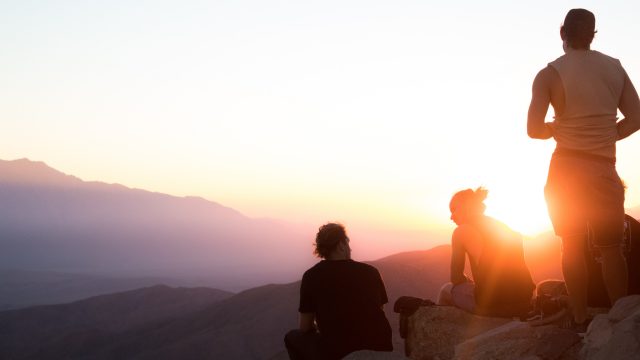 崖の上から夕陽を眺める3人組